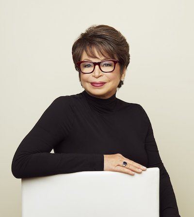 A black woman with light brown skin and short brown hair wearing blackrimmed glasses and a black turtleneck
